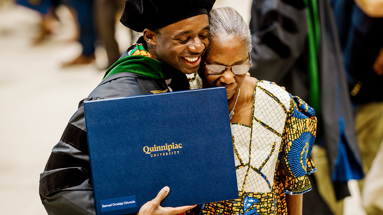 A graduate hugs a relative with their diploma in hand