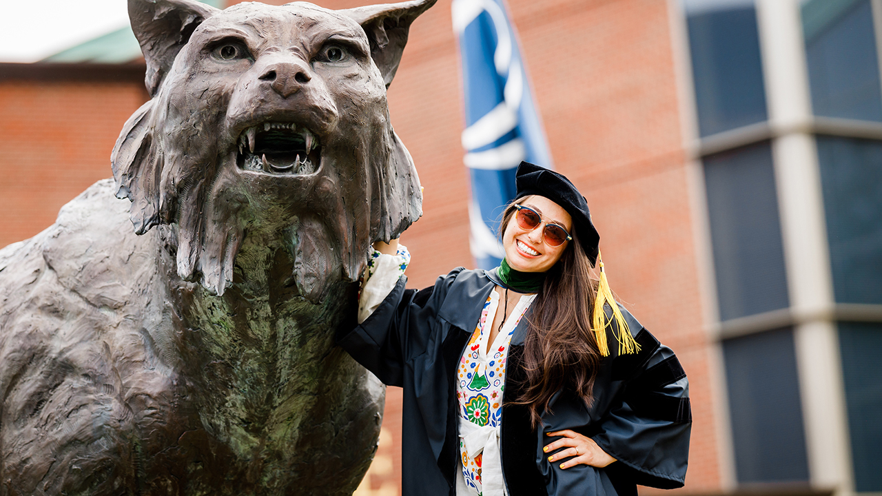 A graduate poses with the bobcat statue and smiles