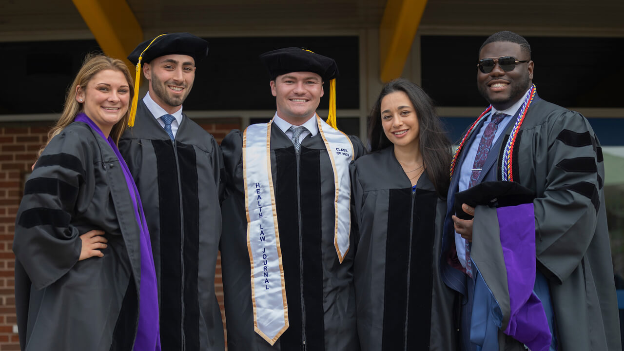 Five graduates stand arm in arm for a photo
