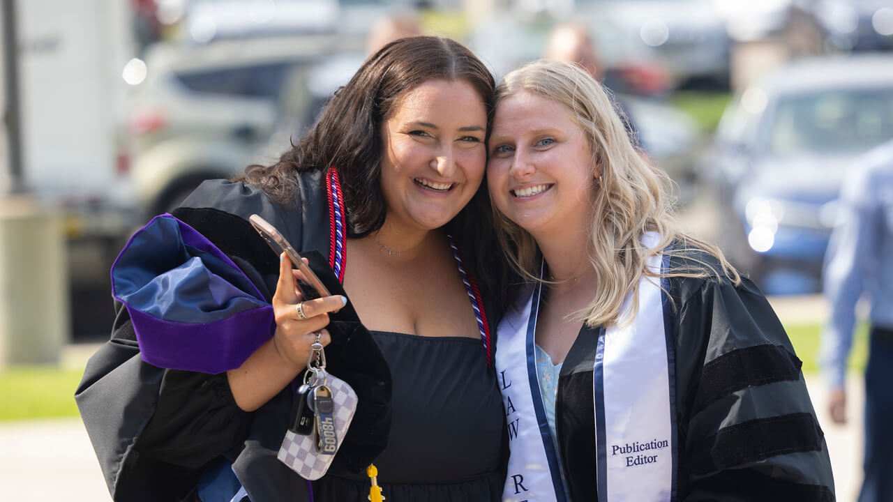 Two graduates hug and smile for a photo