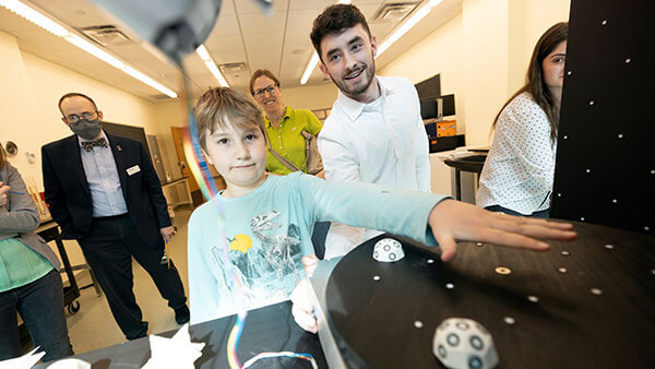A student shows a child how to use their senior project at the School of Computing and Engineering while others watch.