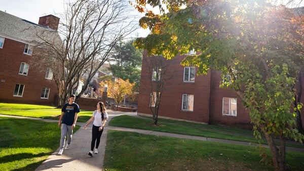 Two students walk behind residence halls on a sunny, fall day