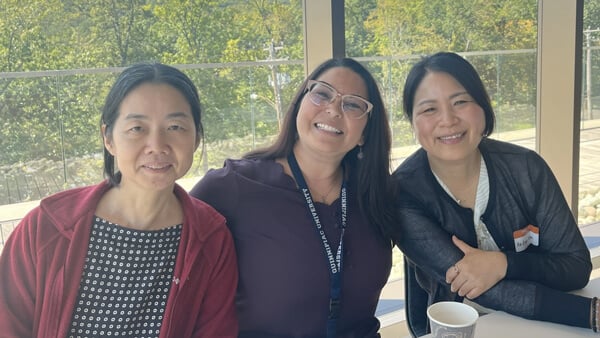 Three Asian women smile for a photo during the Asian Affinity Group meeting