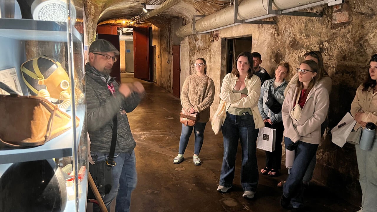 Students in an underground cellar listening to tour guide explain tools and equipment