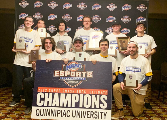 The Quinnipiac eSports team holds trophies and smiles in front of the MAAC championships logo.