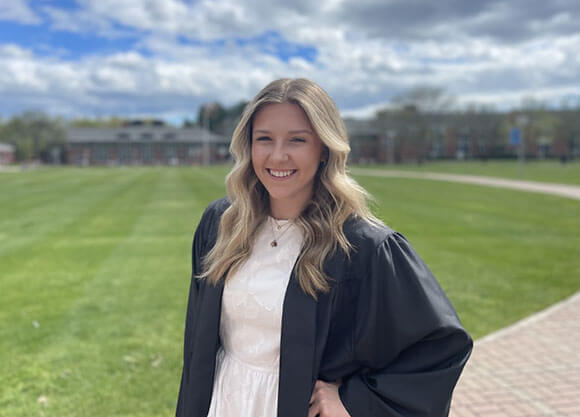 Madison Badalamente smiling in a white dress and graduation gown
