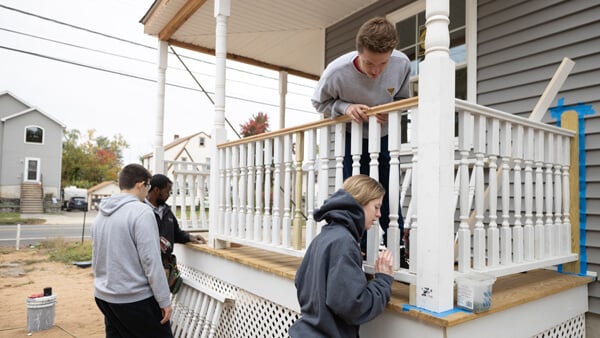 Four students work on repairing a porch railing in a urban area