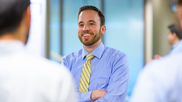 A student in a shirt and tie smiles and talks with people during a conference