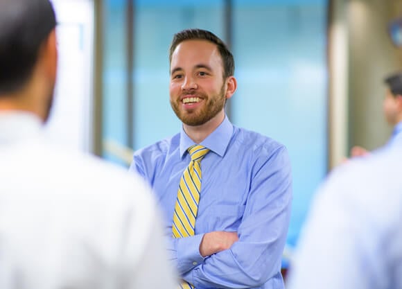 A student in a shirt and tie smiles and talks with people during a conference