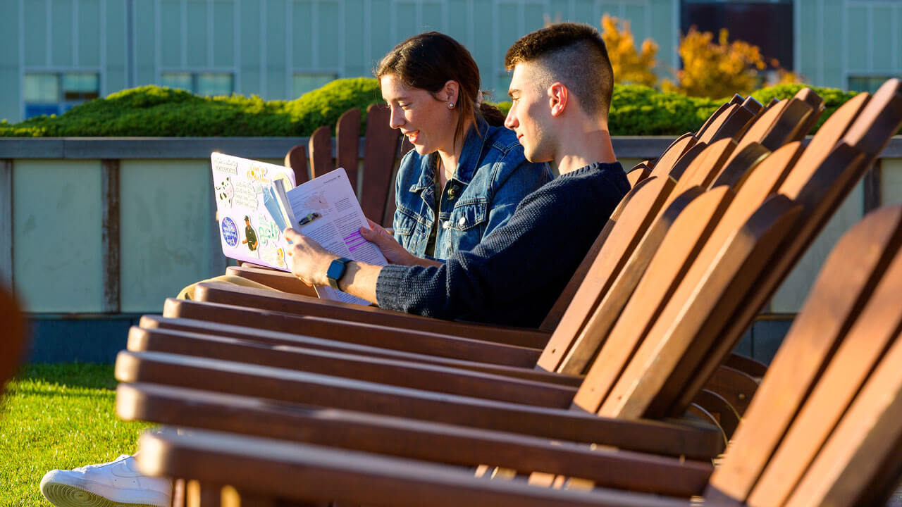 Two students sitting in wooden Adirondack chairs studying