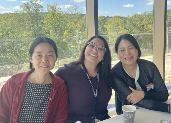 Three Asian women smile for a photo during the Asian Affinity Group meeting
