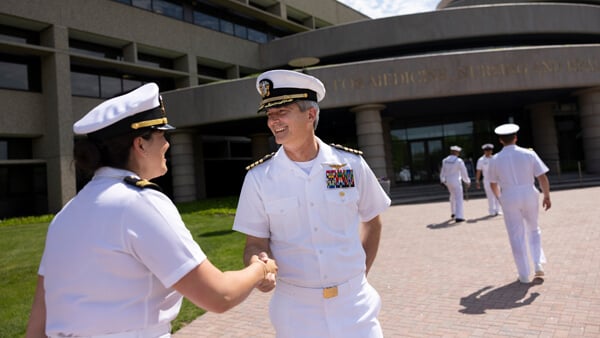 A student in a military uniform shakes hands with the director for veterans affairs outside