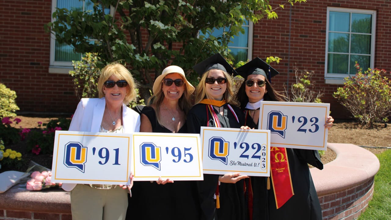 Four alumnae stand with signs displaying their graduation years