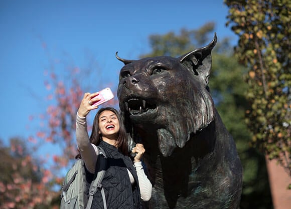 Student takes a selfie with the Bobcat statue on the Mount Carmel Campus