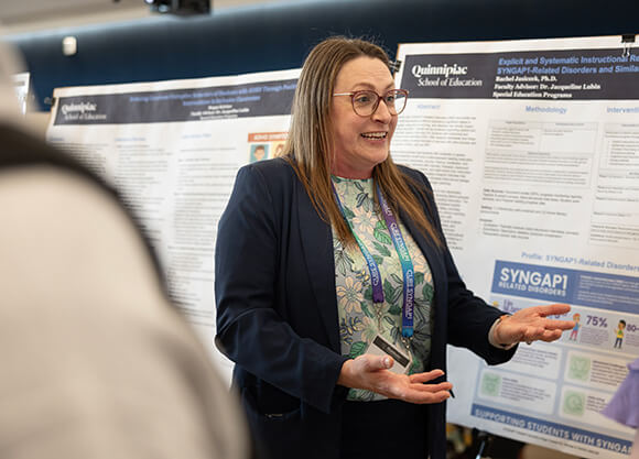 Rachel Jasiczek speaking in front of a poster to someone off camera