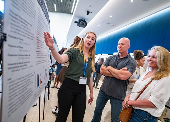 Maya Weathers gesturing to a poster, talking to a man and a woman