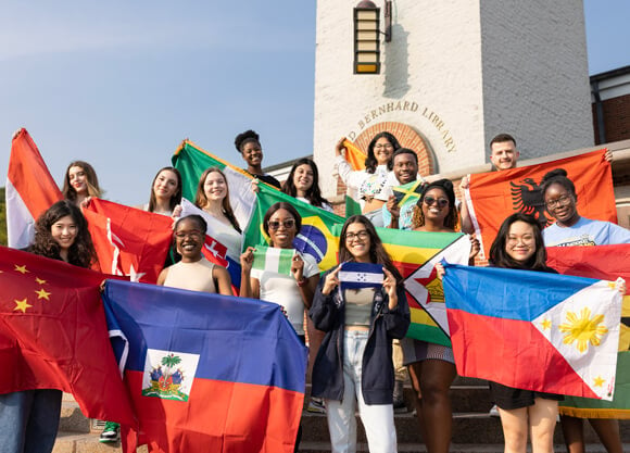 15 international students hold flags of their home countries on the Arnold Bernhard steps