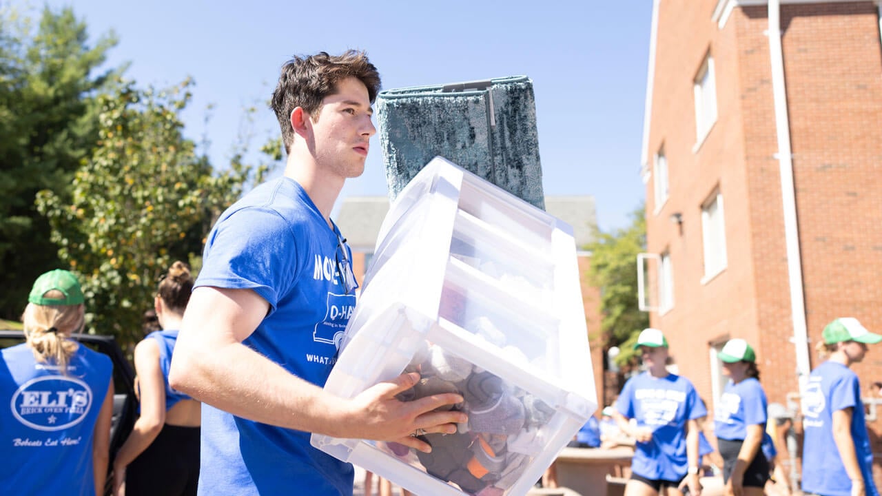 Man carrying box with students outside helping move-in first years