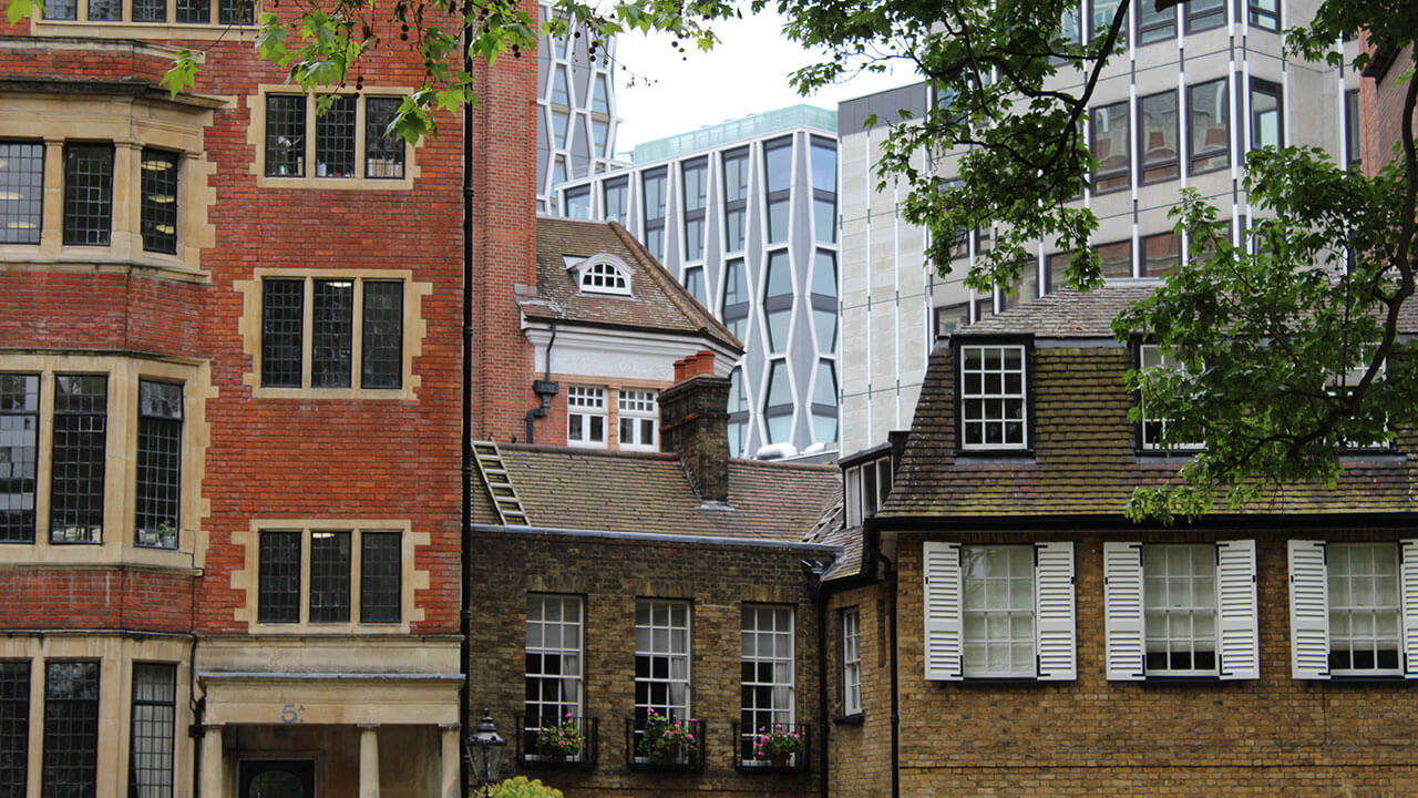 three brick buildings are in the forefront, a modern glass building is behind them