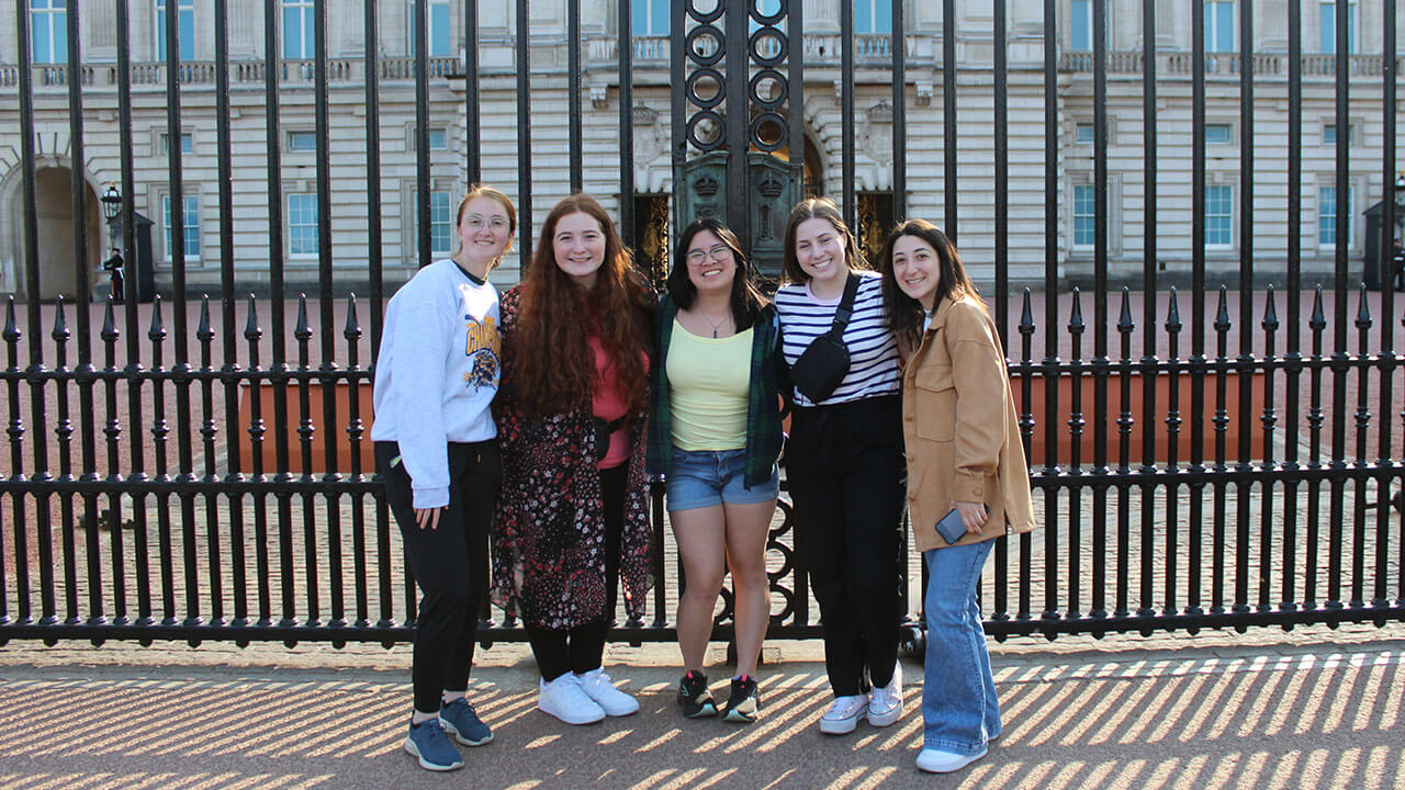 five students pose in front of the gates at buckingham palace