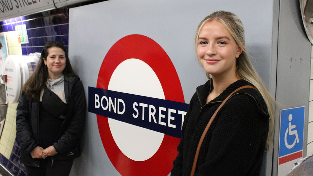 student and professor smile in front of an underground sign for bond street