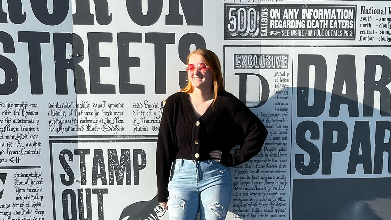 student poses smiling in front of a magazine print wall
