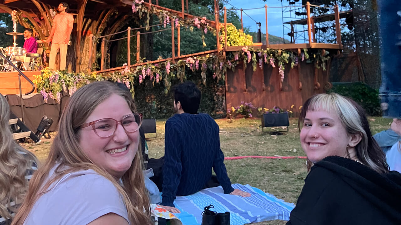 A close-up of two students watching a Shakespeare in the Park performance.