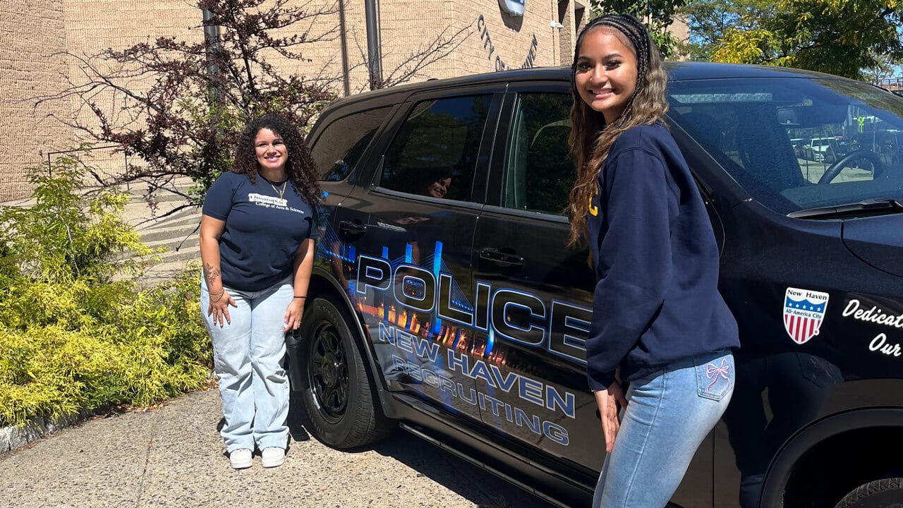 Two female students stand on either side of a New Haven Police car.