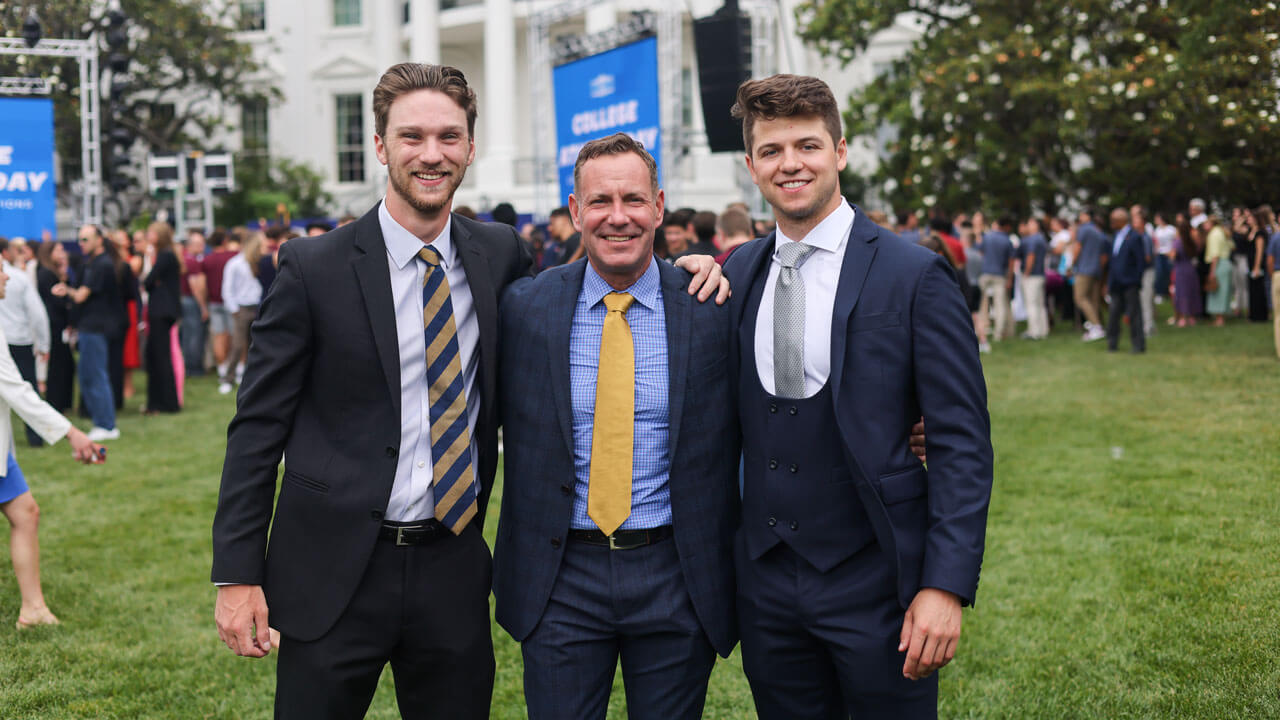 Hockey players wearing blue and gold smiling in front of white house