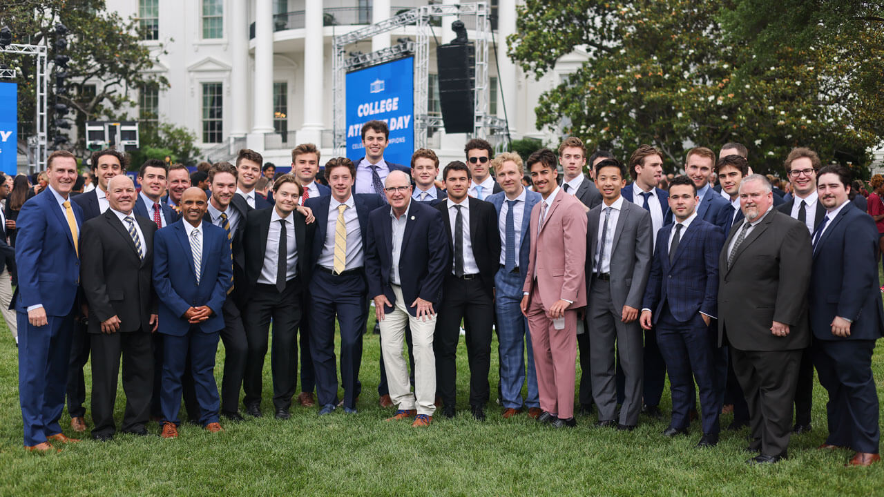 Entire hockey team and coaches standing and smiling in front of the white house