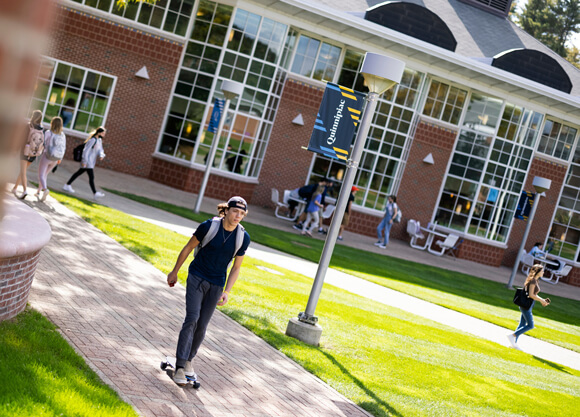 A student on a skateboard and several other students walk in front of the student center in the fall