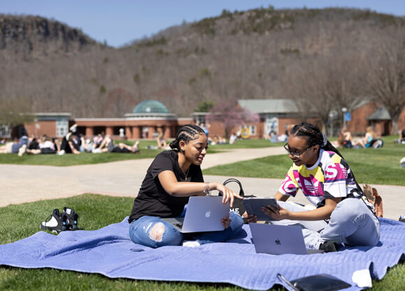 Two students sit on a blanket and study among dozens of students on the quad on a spring day