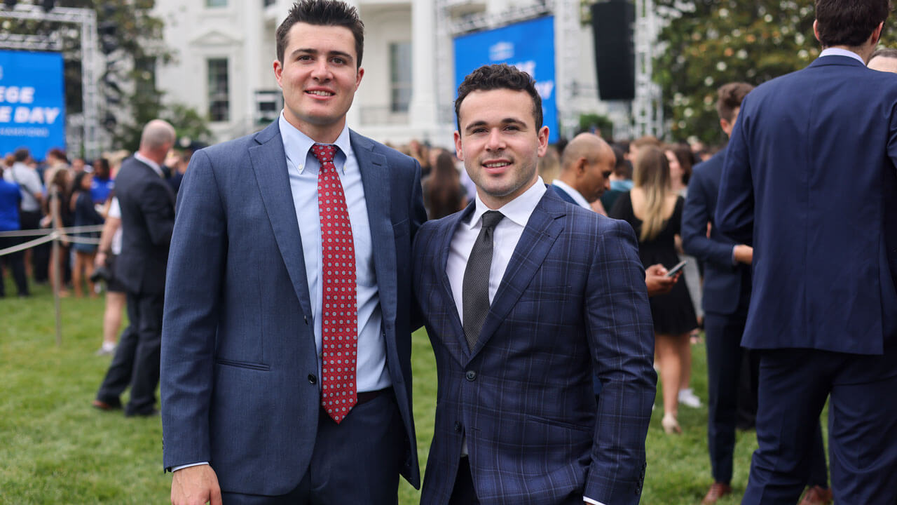 Two hockey players smiling with the white house behind them