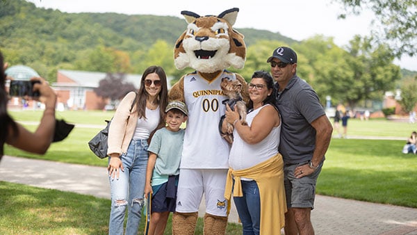 group of four people and a small dog pose with Boomer the Quinnipiac mascot