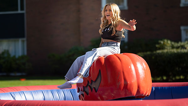 student sits on a pumpkin that is tilting to the side