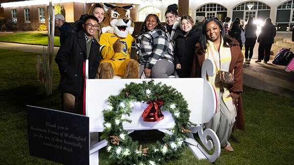 group of six poses with Boomer the mascot in a white sleigh with a wreath on it