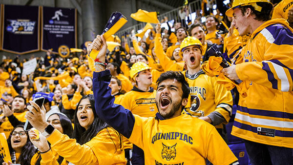 crowd wearing game day gold Quinnipiac shirts waves rally towels and cheers