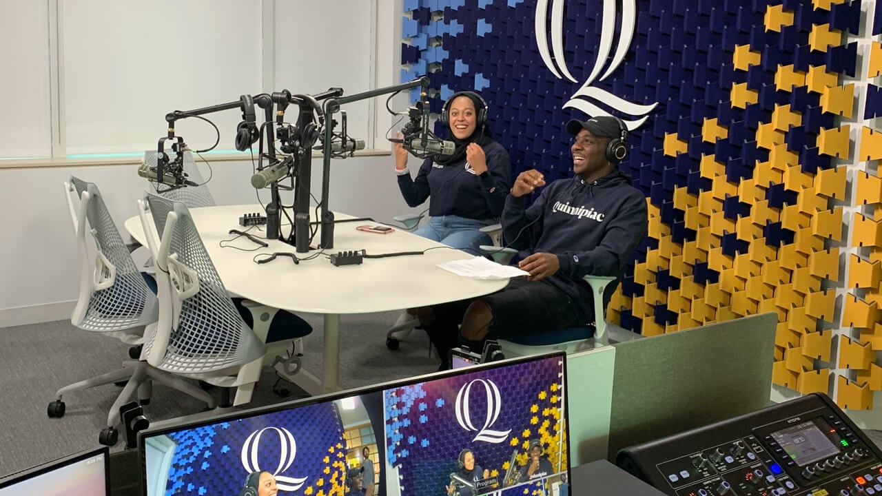 Two communications students in Quinnipiac sweatshirts work in the podcast studio
