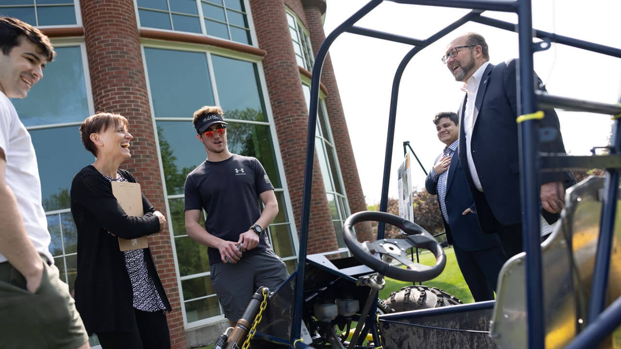 Professors and students observe a student project dune buggy.