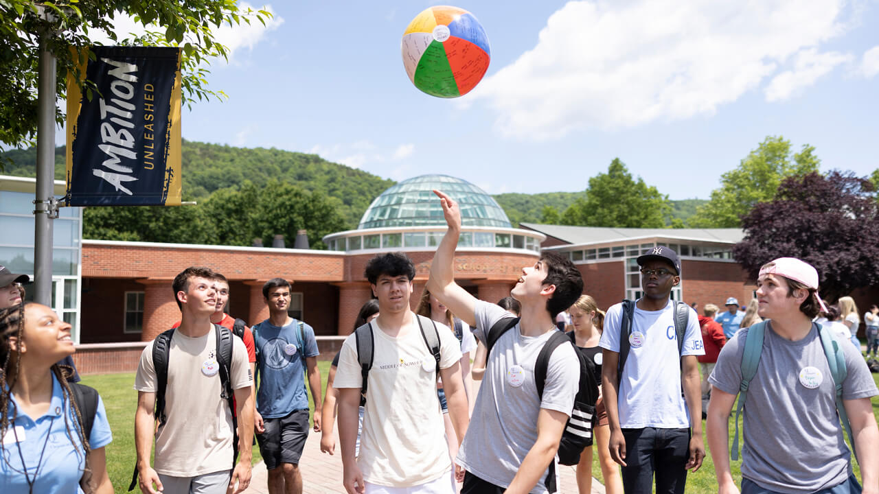 An Orientation group walks across the quad, one student tosses a beach ball in the air