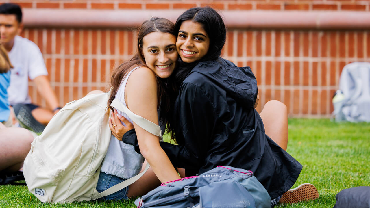 Two new students hug as they sit on the quad during Orientation