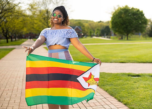 Reinett Chefu smiling with a Zimbabwe flag in a grassy area