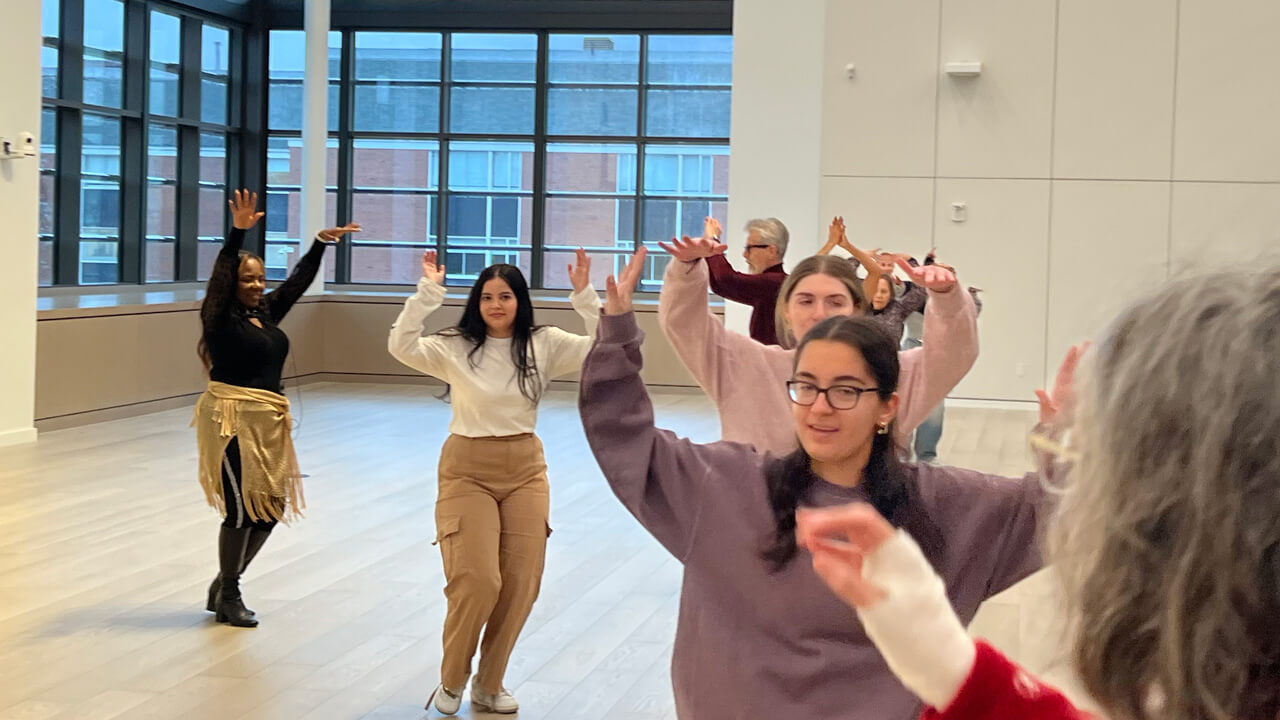 A line of students and faculty members with their arms up as the instructor demonstrates a salsa move.