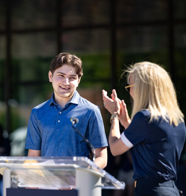 SGA president stands at a podium and smiles at President Hardin while she claps