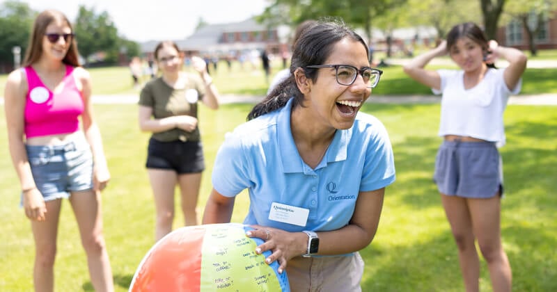 An Orientation leader laughs as she holds a beach ball during game with new students