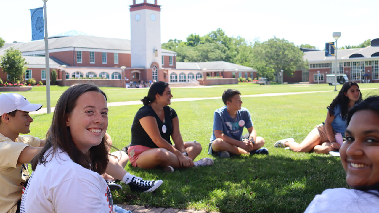 A new student smiles as she sits with her Orientation group in a circle on the quad