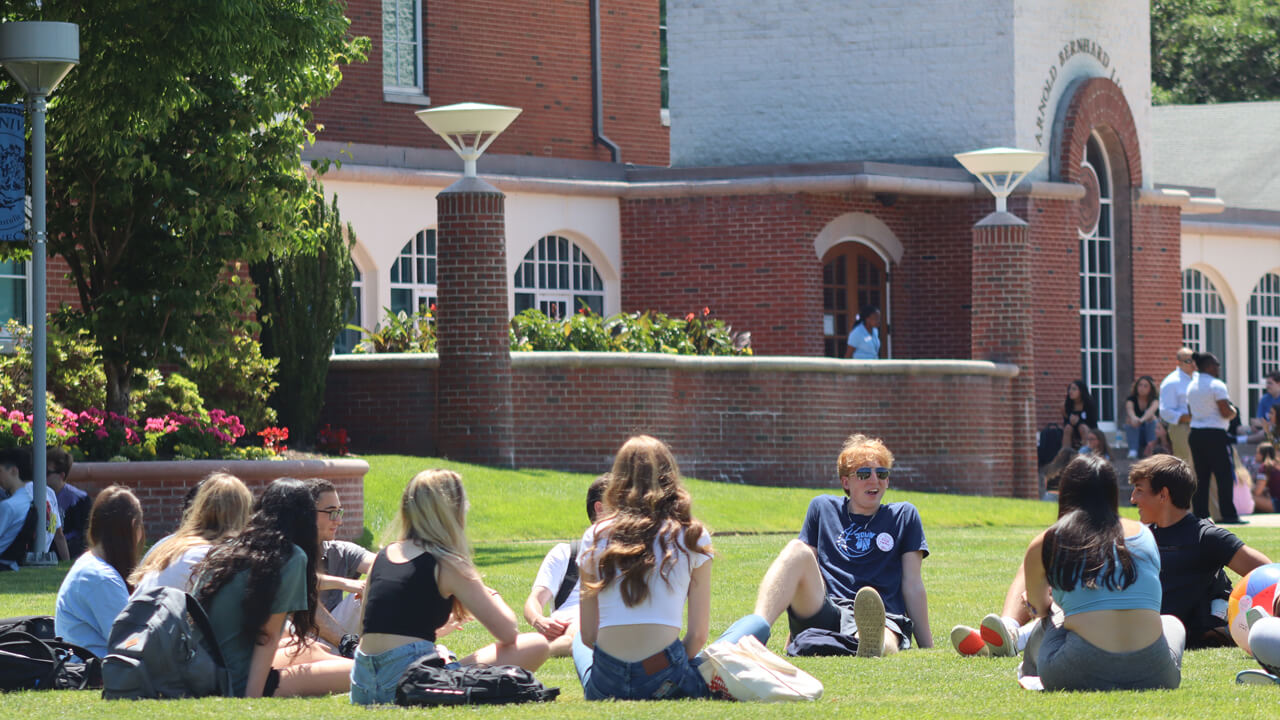 An Orientation group sits in a circle on the grass in front of the library