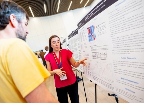 Photo of Kaitlyn McVeigh standing in front of poster project and presenting her work to a male listener