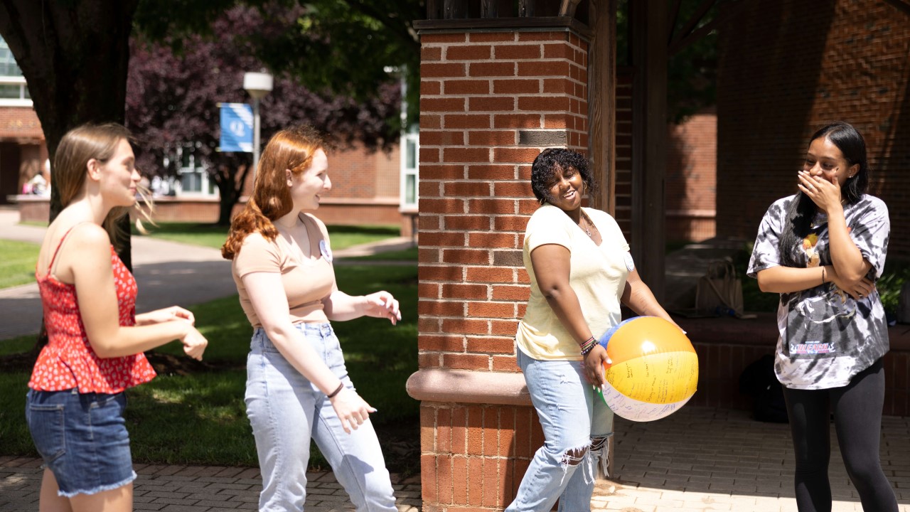 Four students laugh as they play with a beach ball.