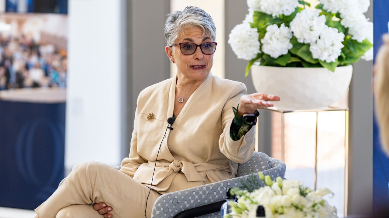 Fran Pastore speaking while sitting in a chair in front of a vase of flowers.